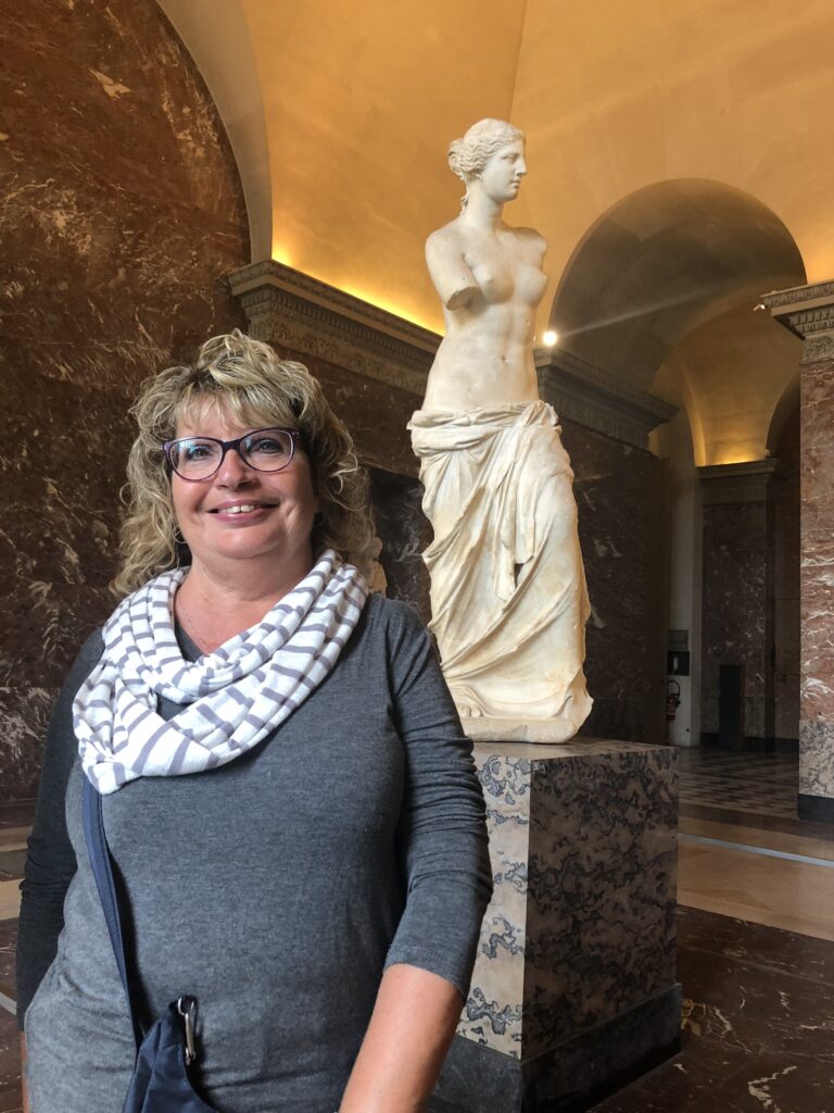 Jeannette standing in the Louvre Museum in Paris with the Venus de Milo sculpture