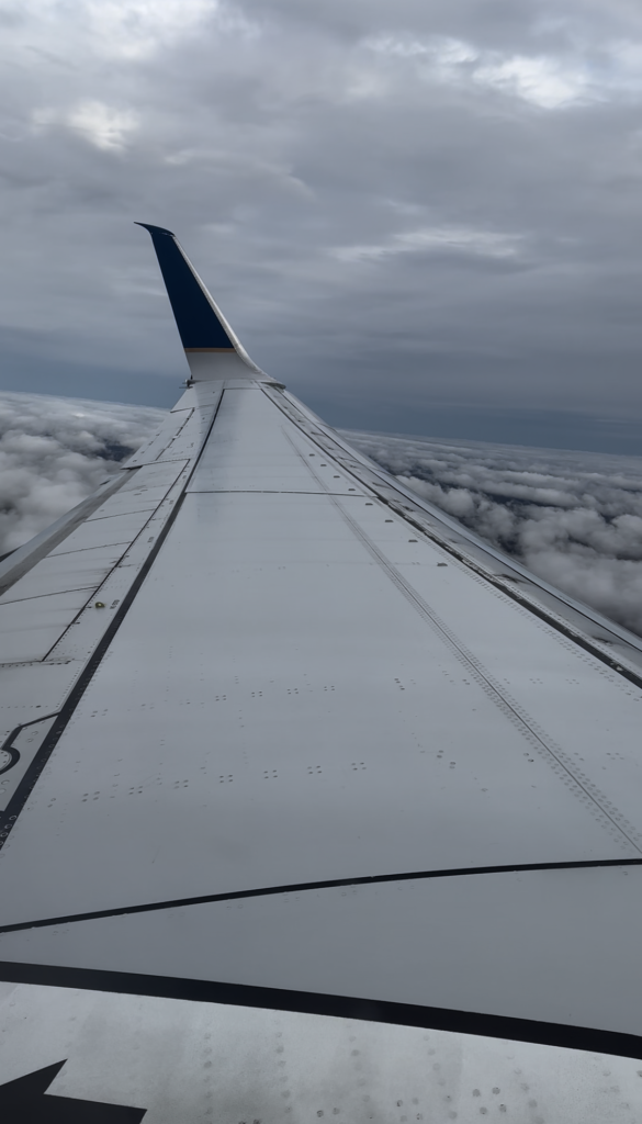 United Airlines wing view above the clouds during a flight to a vacation destination